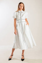 A solid white woven midi dress featuring collar, button down, short puff sleeve, contrasting piping detail and full skirt