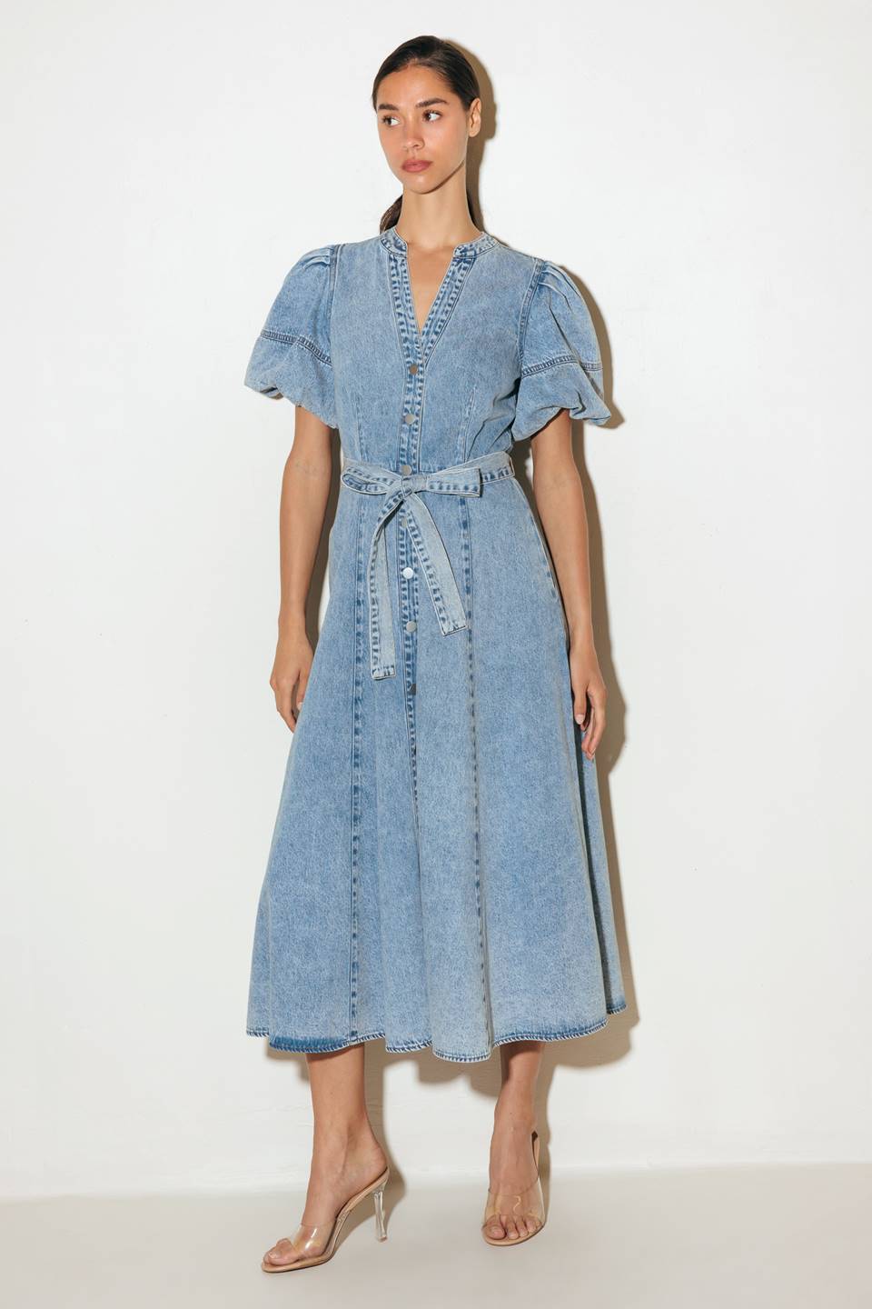 A washed denim midi dress featuring china collar, front button down, short puff sleeve, self sash and full skirt.
