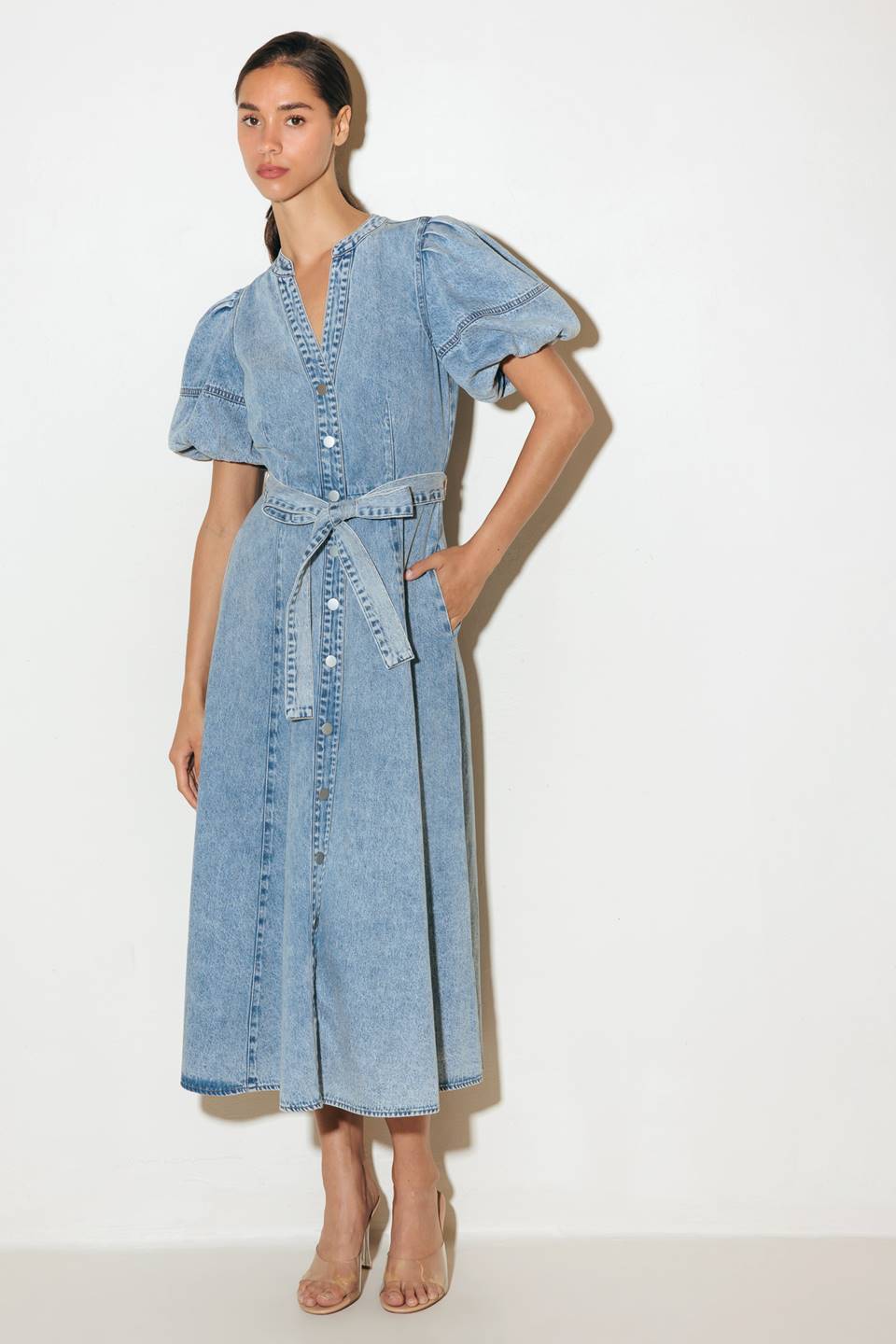 A washed denim midi dress featuring china collar, front button down, short puff sleeve, self sash and full skirt.