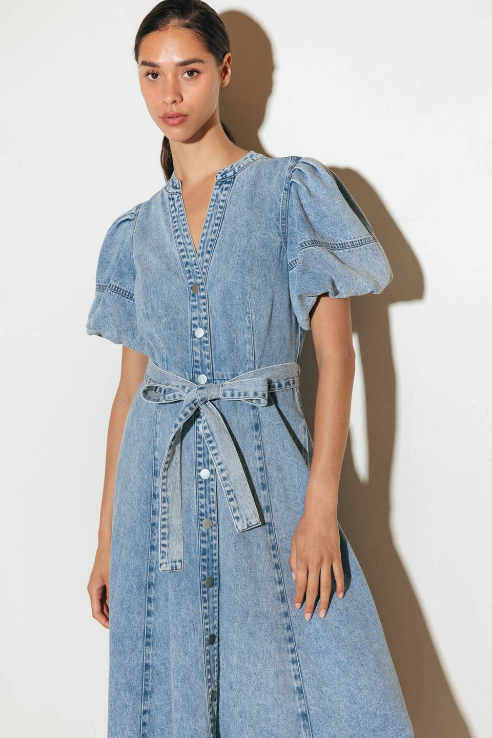 A washed denim midi dress featuring china collar, front button down, short puff sleeve, self sash and full skirt.