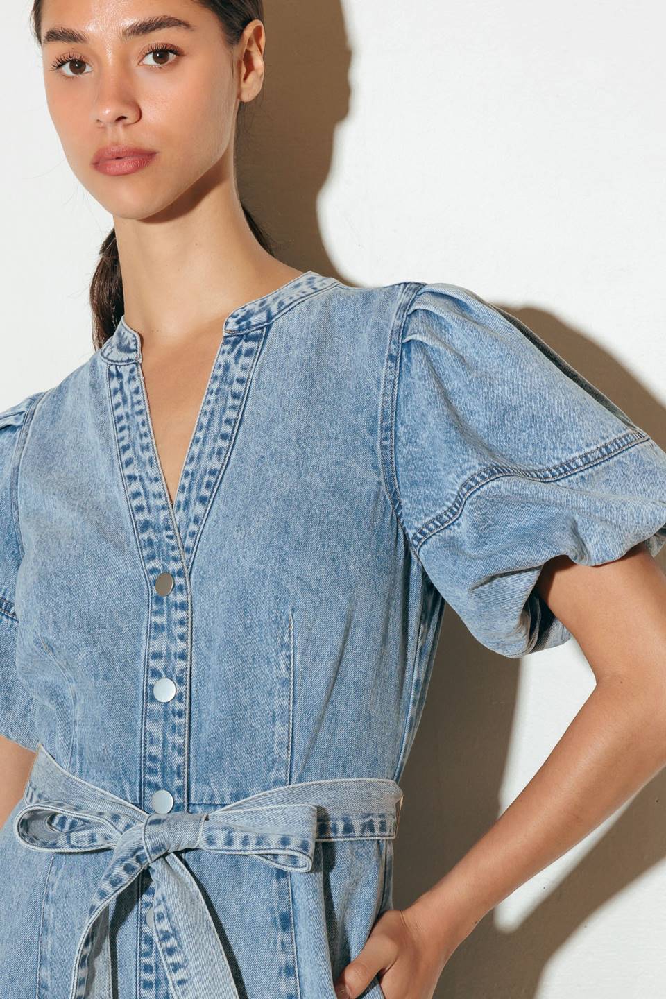 A washed denim midi dress featuring china collar, front button down, short puff sleeve, self sash and full skirt.