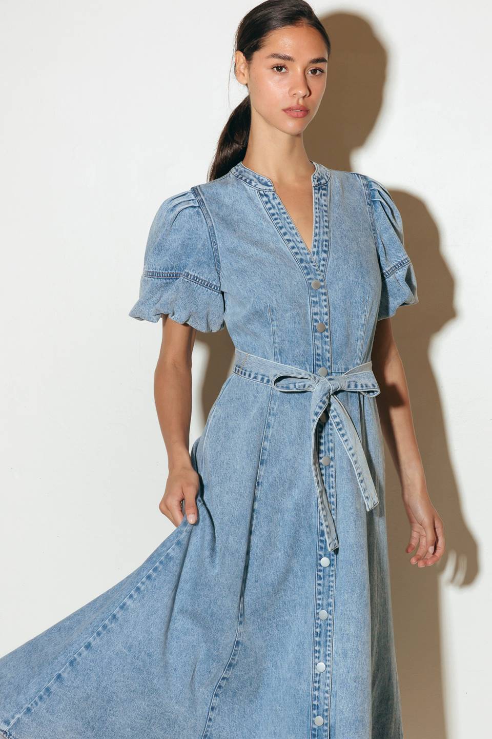 A washed denim midi dress featuring china collar, front button down, short puff sleeve, self sash and full skirt.