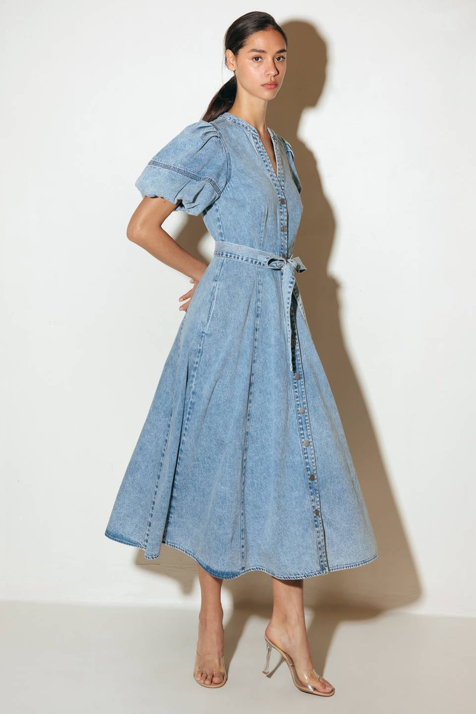 A washed denim midi dress featuring china collar, front button down, short puff sleeve, self sash and full skirt.