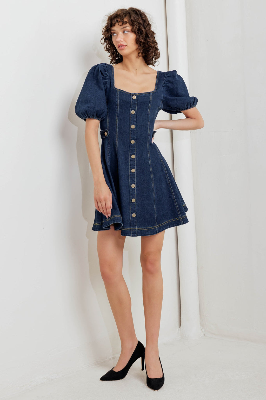 A washed denim mini dress featuring square neckline, short puff sleeve, button down detail, circle skirt and back zipper closure
