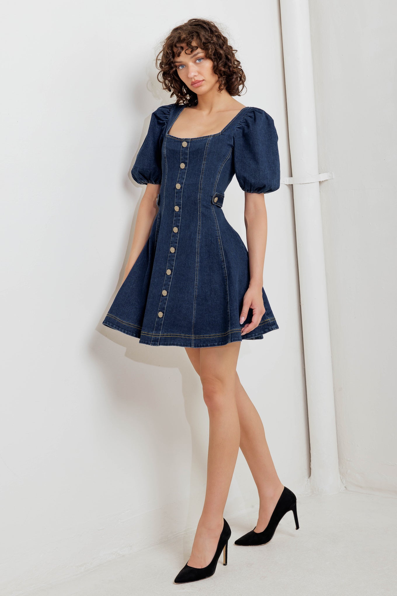 A washed denim mini dress featuring square neckline, short puff sleeve, button down detail, circle skirt and back zipper closure