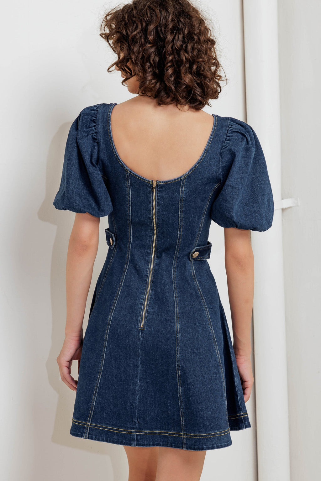 A washed denim mini dress featuring square neckline, short puff sleeve, button down detail, circle skirt and back zipper closure