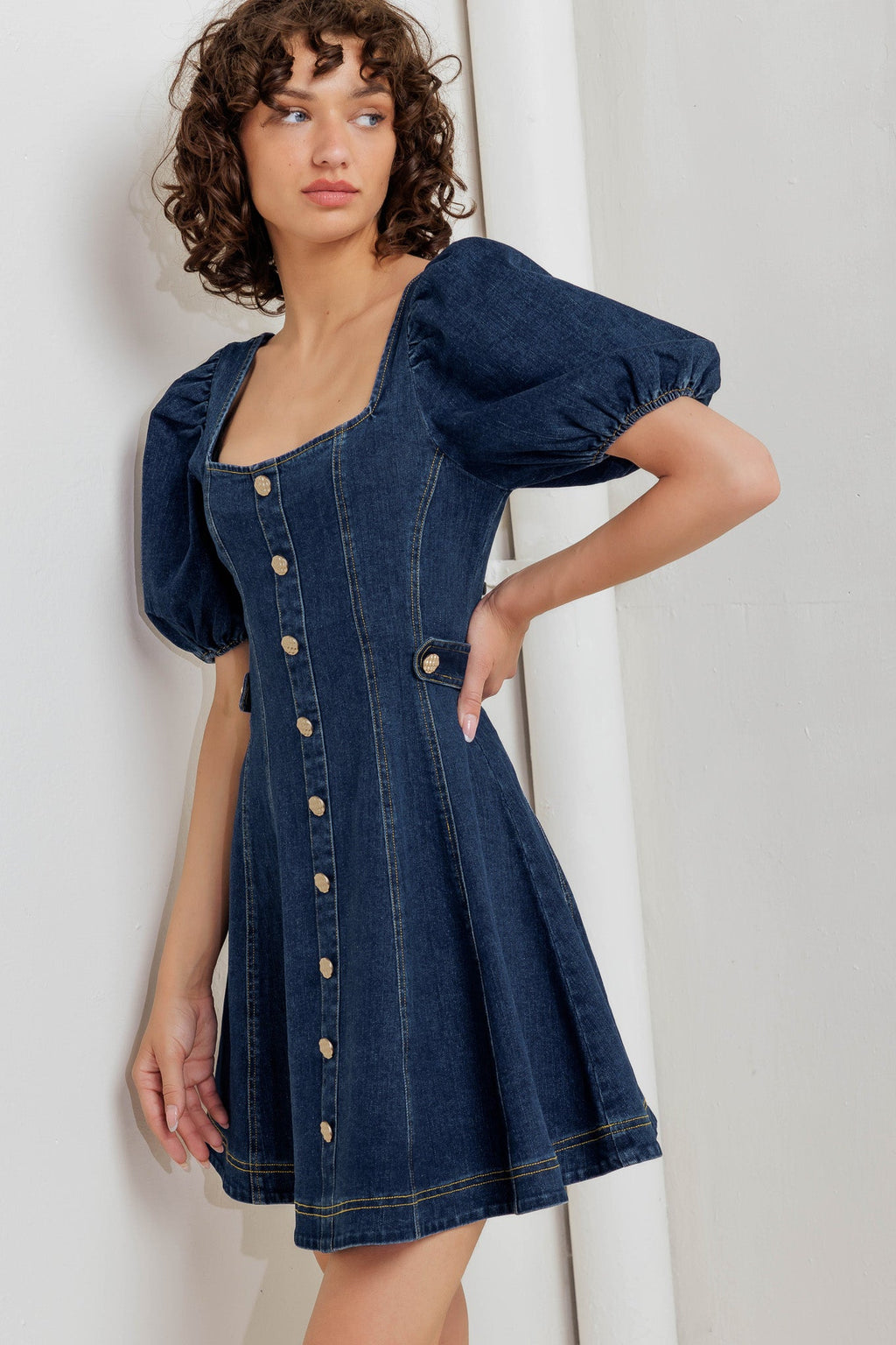 A washed denim mini dress featuring square neckline, short puff sleeve, button down detail, circle skirt and back zipper closure