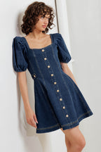 A washed denim mini dress featuring square neckline, short puff sleeve, button down detail, circle skirt and back zipper closure