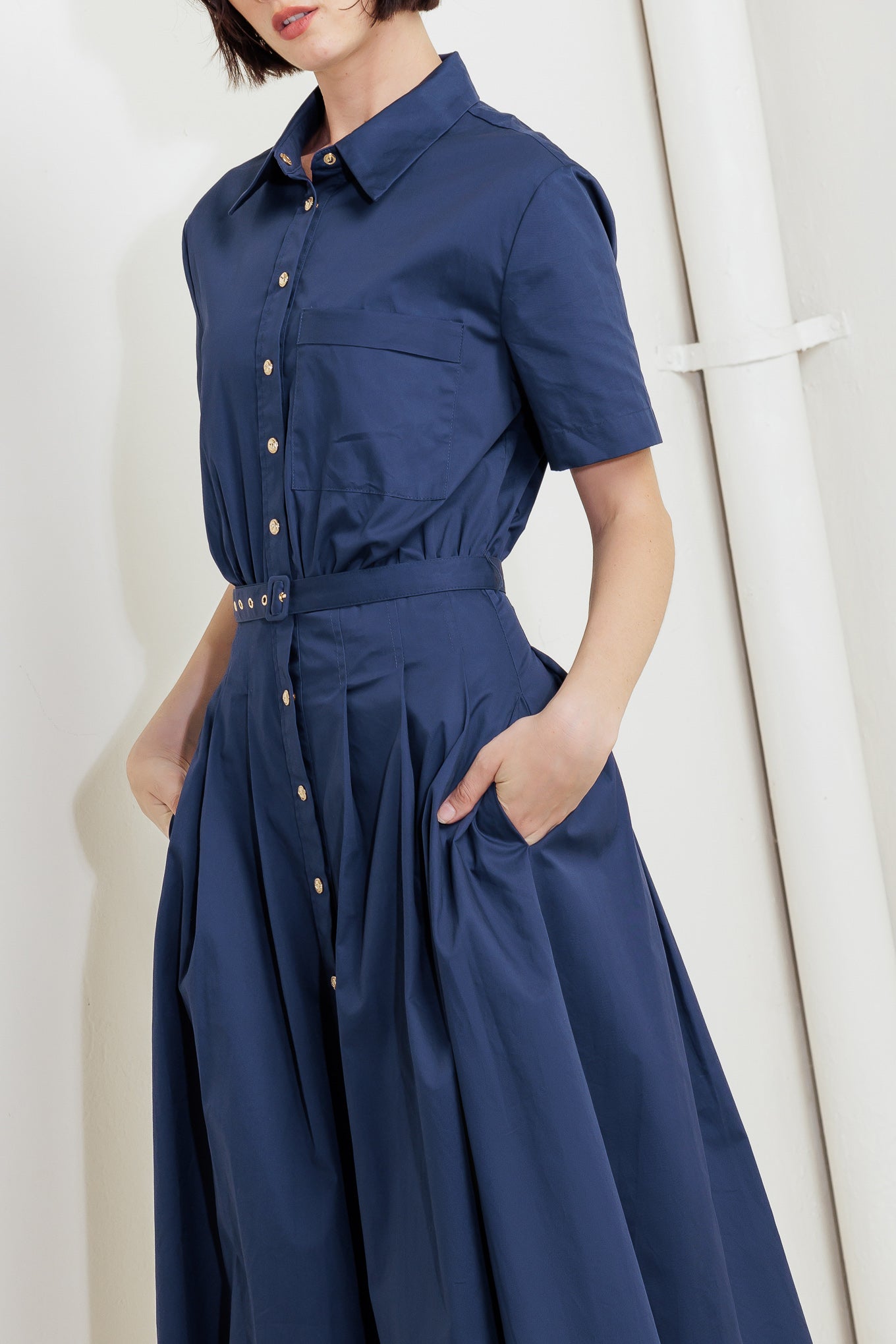 A solid woven midi dress featuring collar, short sleeve, front pocket, button down, self-belt and full skirt