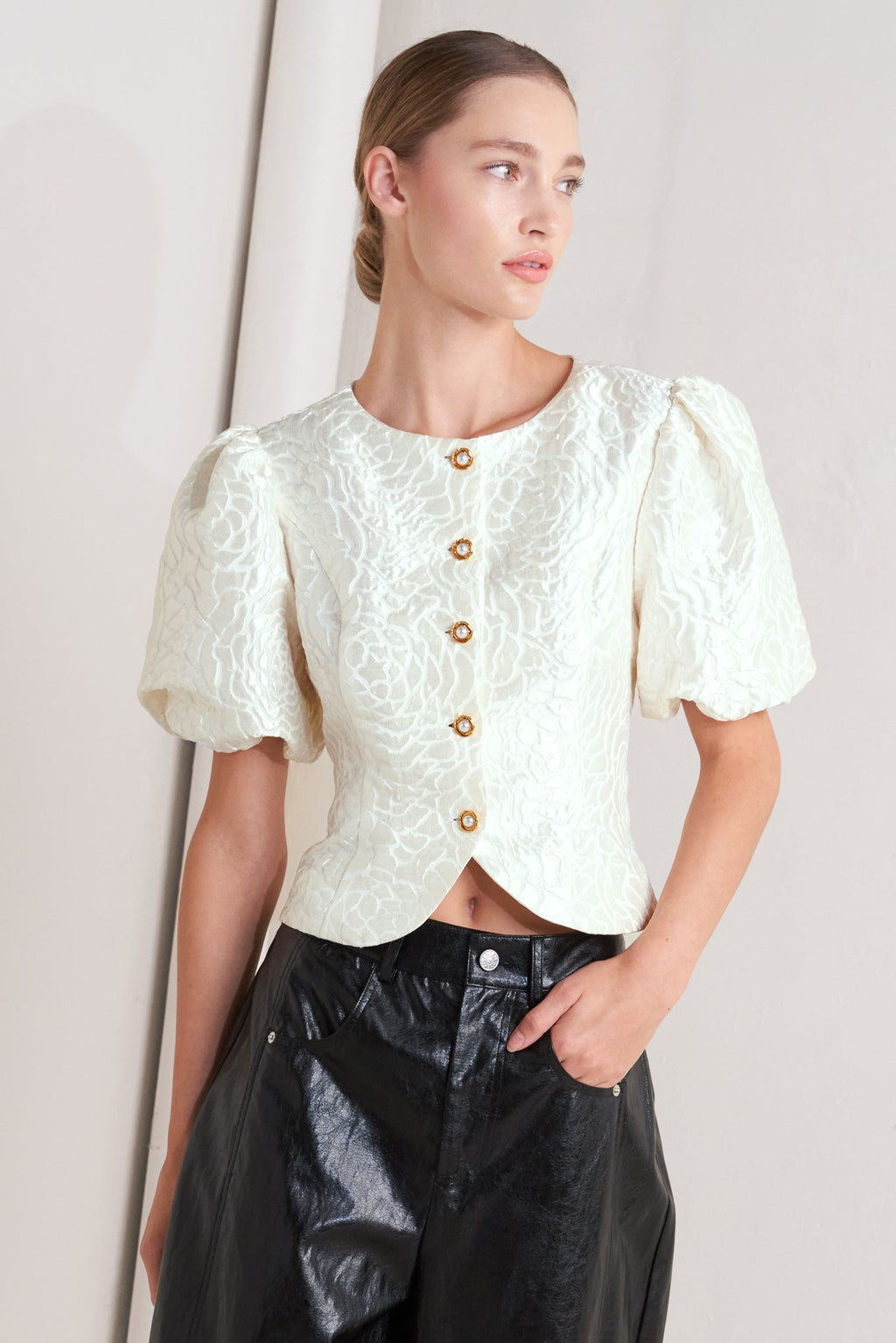 A textured woven top featuring round neckline, short puff sleeve and front button down
