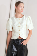 A textured woven top featuring round neckline, short puff sleeve and front button down