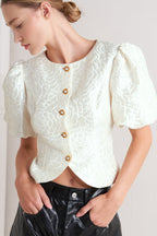 A textured woven top featuring round neckline, short puff sleeve and front button down