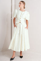 A textured woven top featuring round neckline, short puff sleeve and front button down