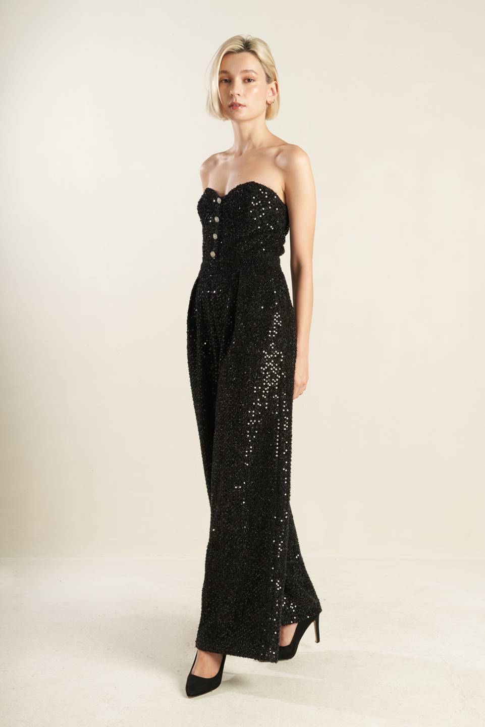 A black sequin jumpsuit featuring, sweetheart neckline, front button detail, side pocket, wide leg and back zipper closure