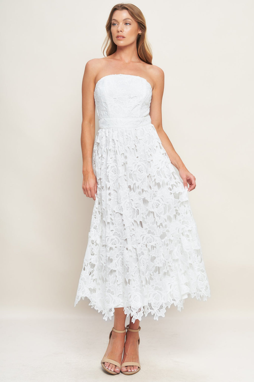An off-white lace midi dress, crafted with intricate weaving and a straight neckline. Adorned with a delicate ruffled hem and complete with a concealed zipper closure at the back.