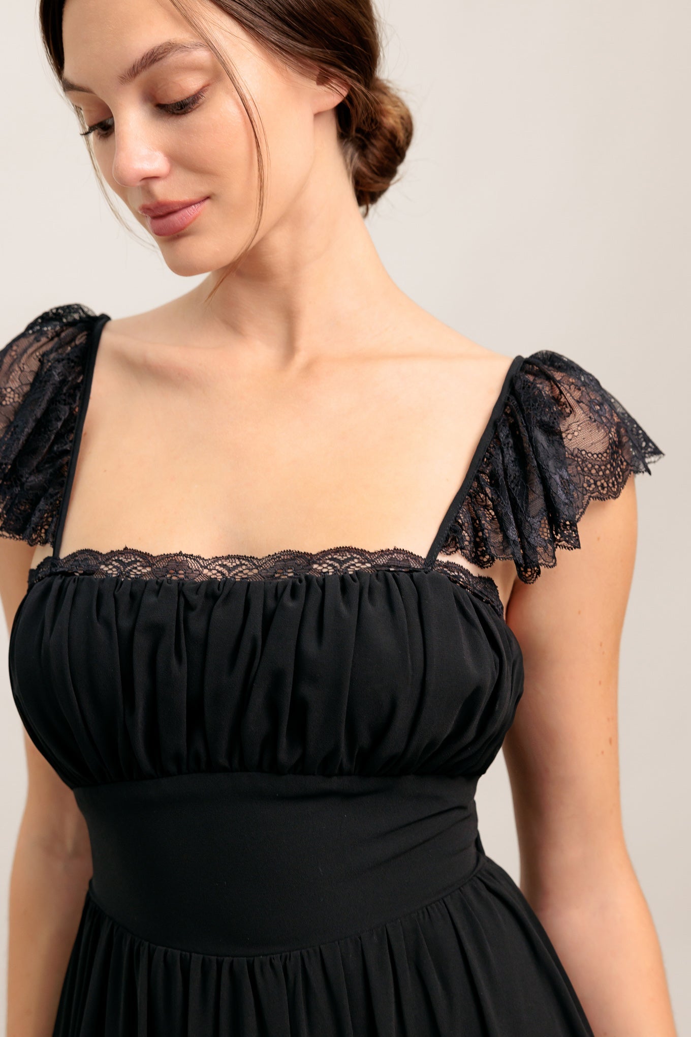 A solid black woven maxi dress featuring straight neckline with lace edge, waist yoke, tiered skirt, bare back with tie closure