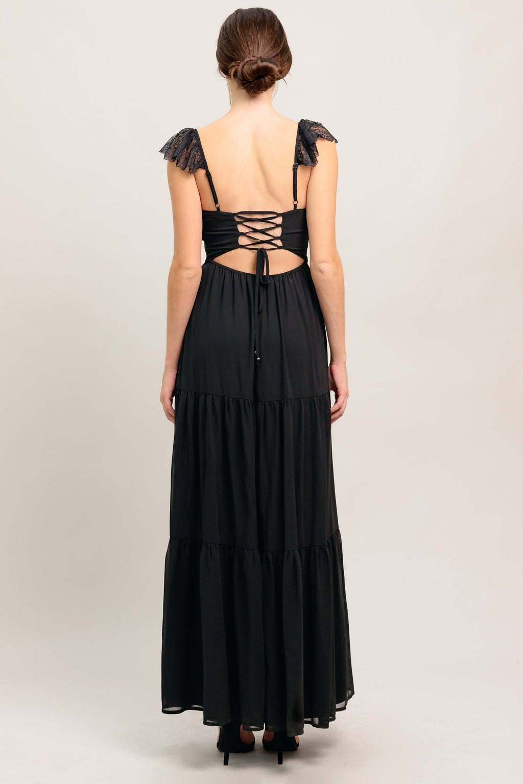 A solid black woven maxi dress featuring straight neckline with lace edge, waist yoke, tiered skirt, bare back with tie closure