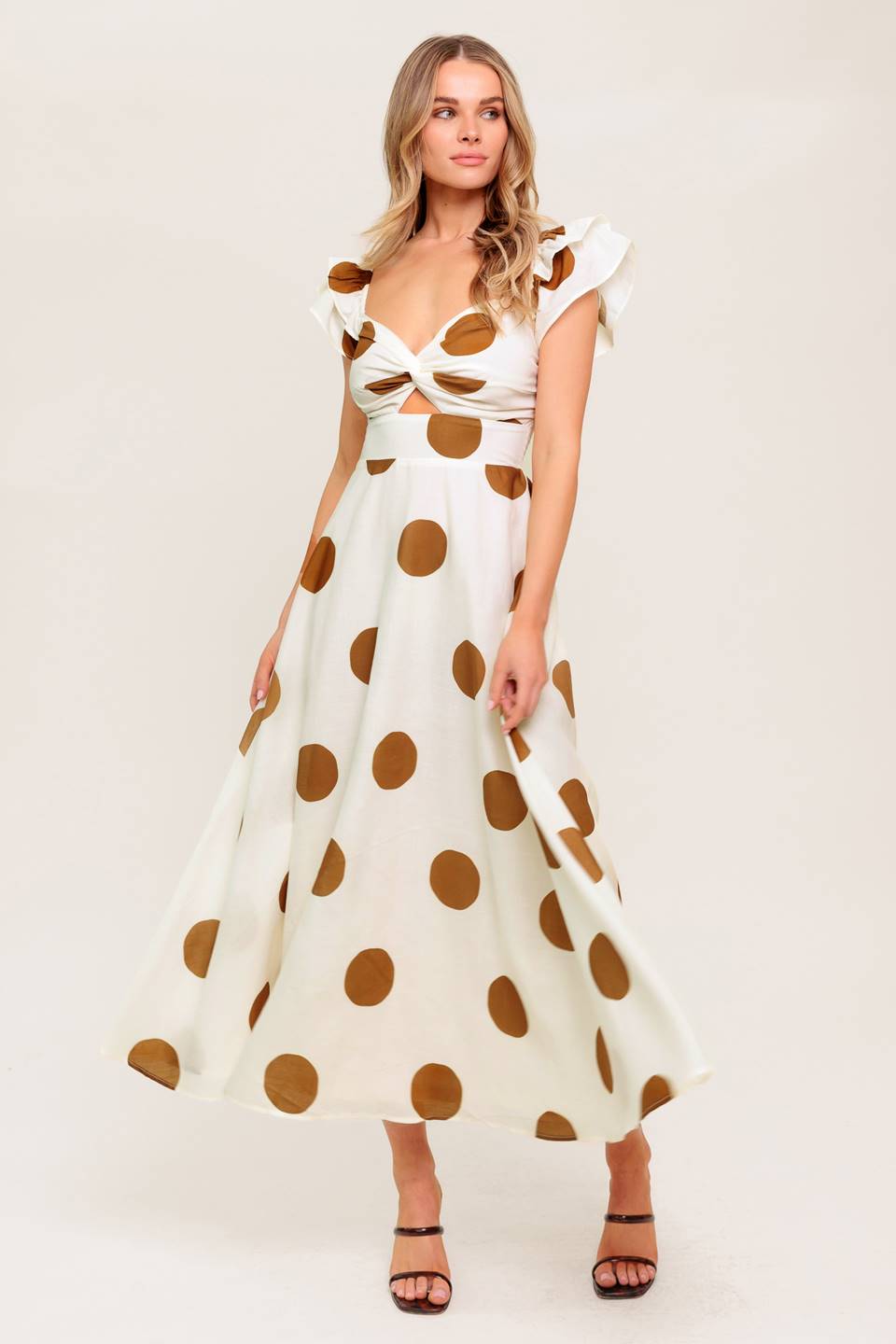 Woman wearing a white dress with brown polka dots on a plain background