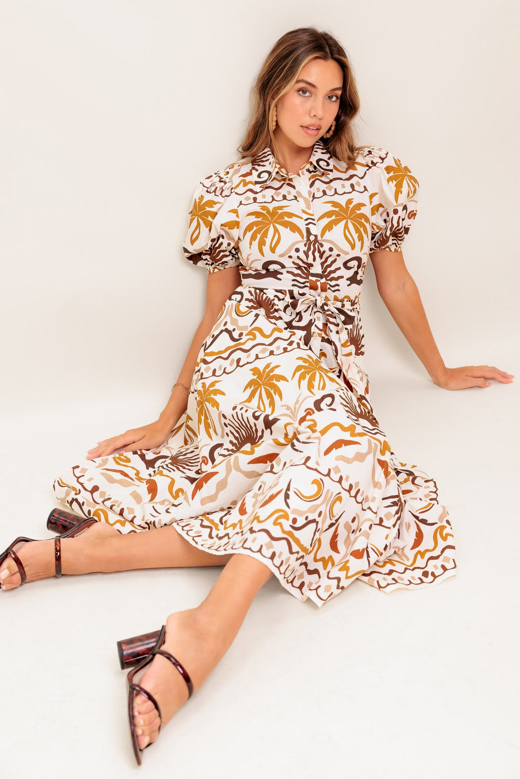 A printed woven midi dress featuring collar, short puff sleeve, button down, self sash and full skirt