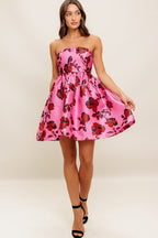 strapless mini dress showcases a pink floral pattern on woven fabric, designed with a full skirt and secured by a back zipper closure.