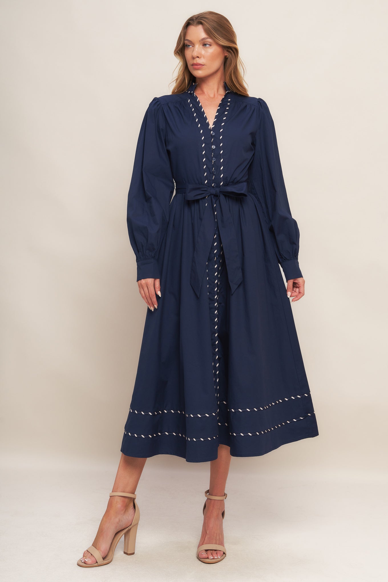 A solid navy woven midi dress featuring high neckline with V front, long sleeve with cuff, self-sash tie, front button down and contrasting binding