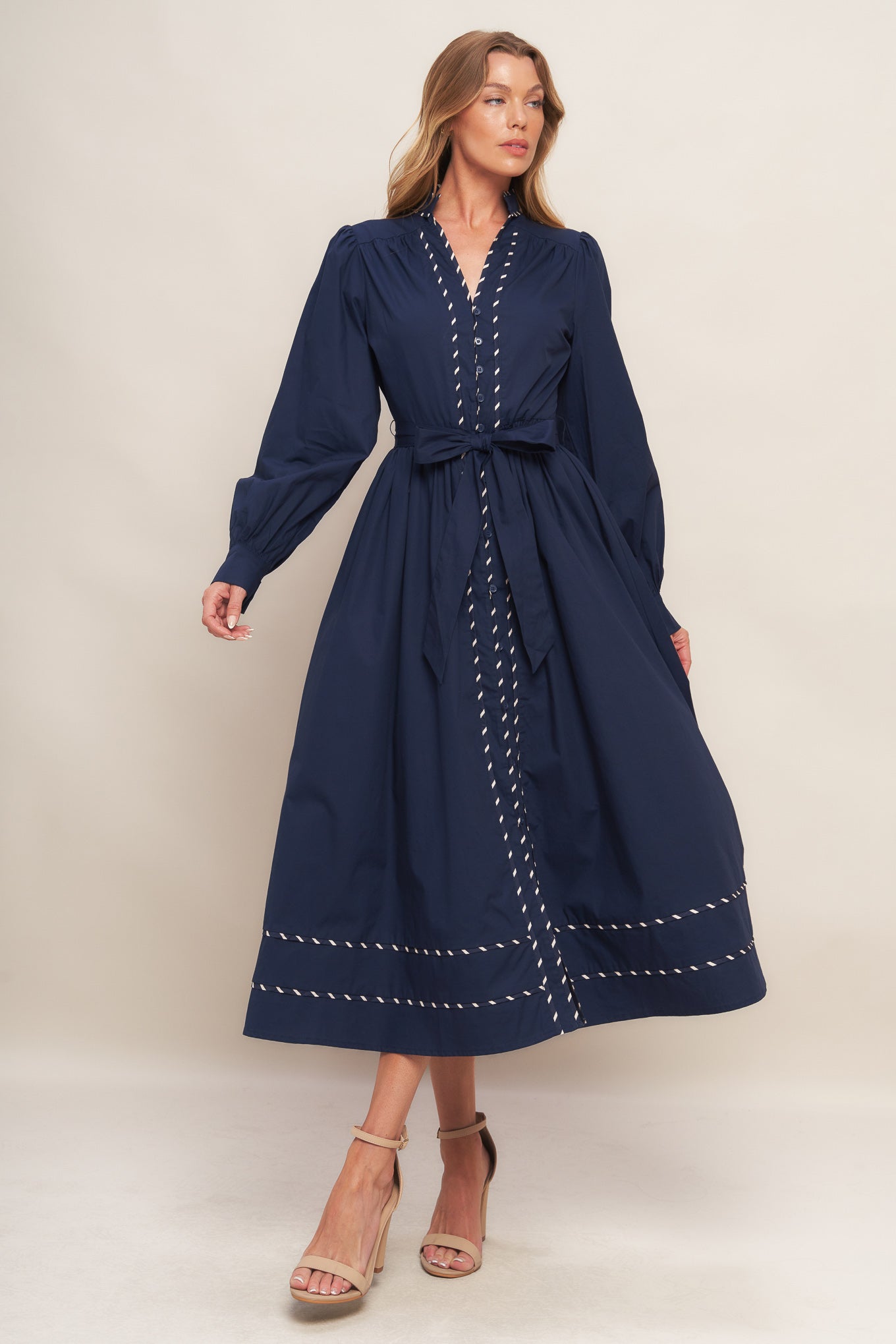 A solid navy woven midi dress featuring high neckline with V front, long sleeve with cuff, self-sash tie, front button down and contrasting binding