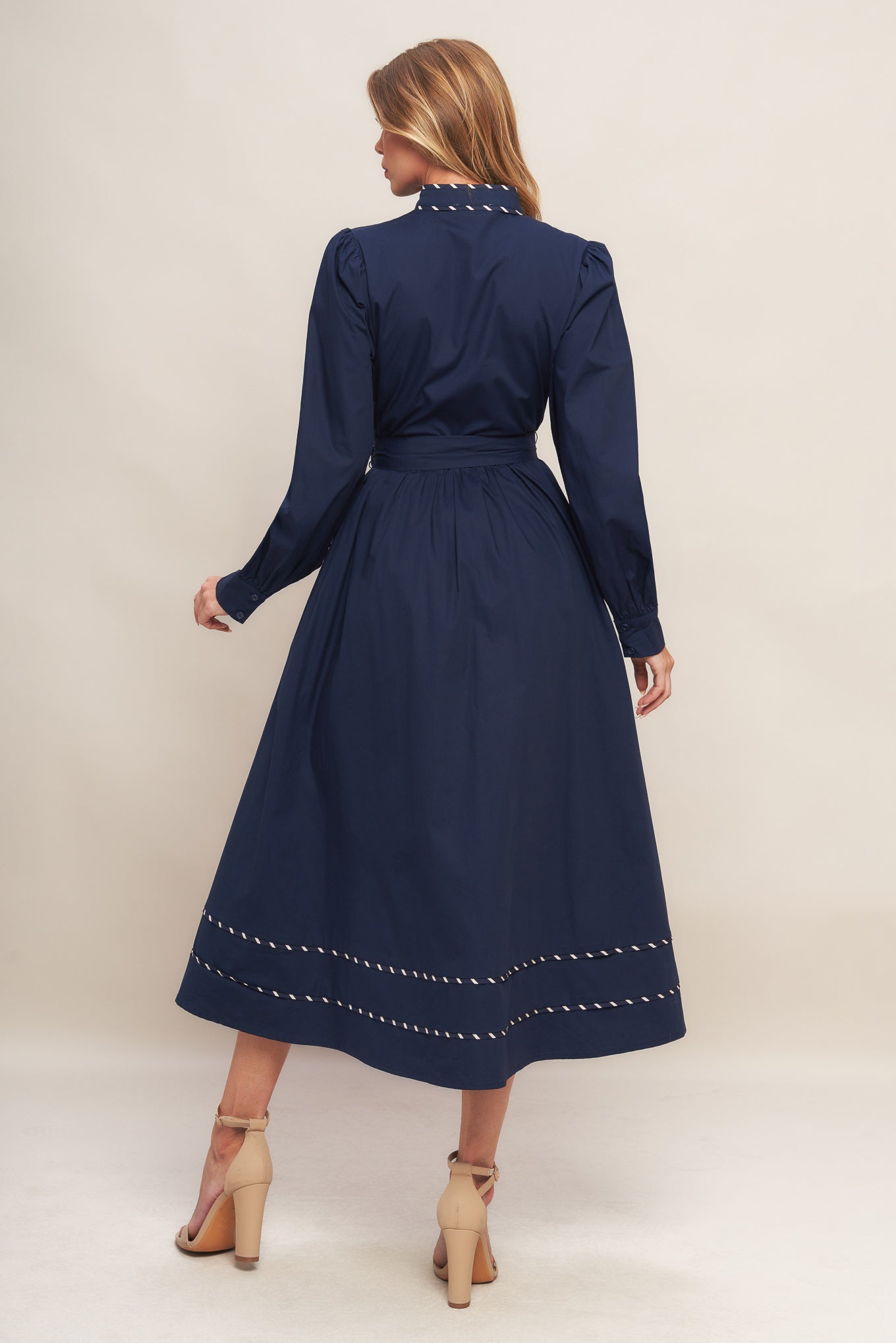 A solid navy woven midi dress featuring high neckline with V front, long sleeve with cuff, self-sash tie, front button down and contrasting binding