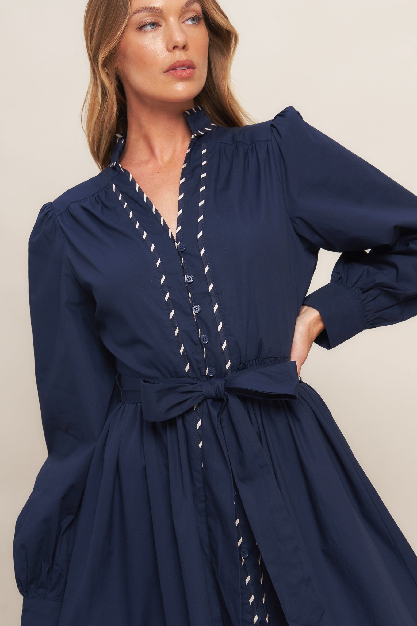 A solid navy woven midi dress featuring high neckline with V front, long sleeve with cuff, self-sash tie, front button down and contrasting binding