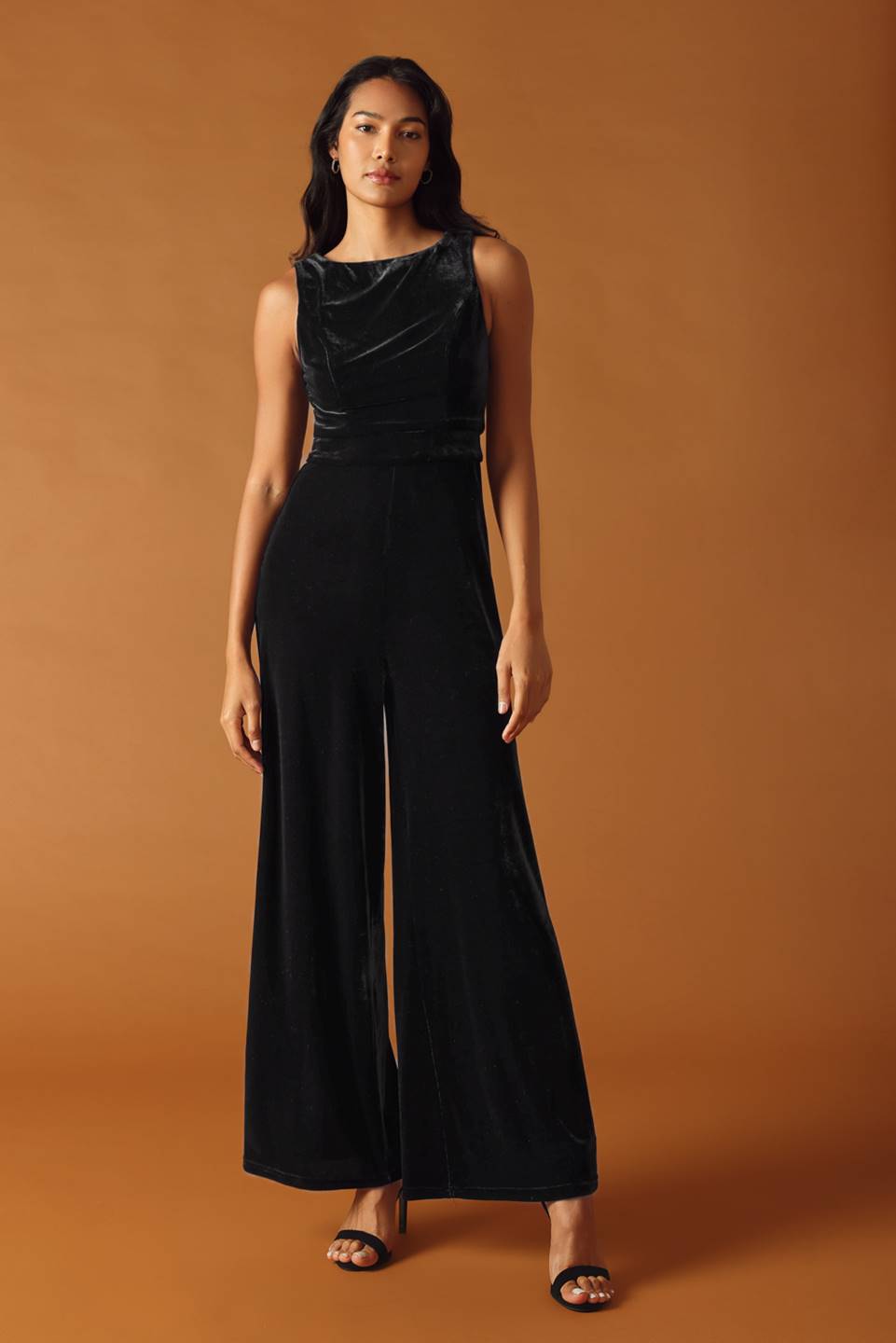 Woman wearing a black jumpsuit against an orange background