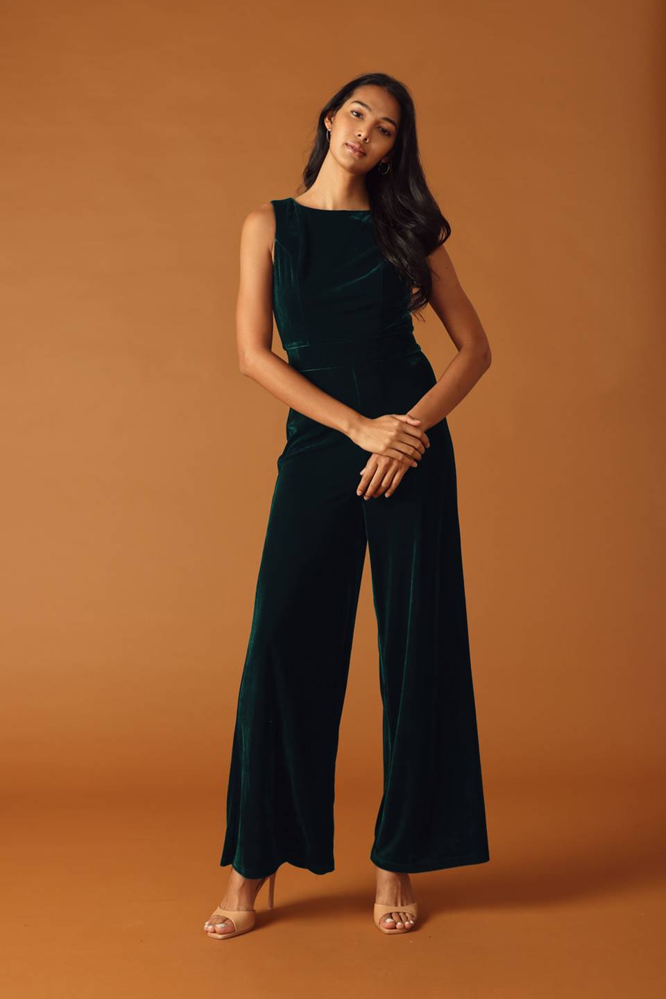 Woman wearing a green velvet jumpsuit against an orange background