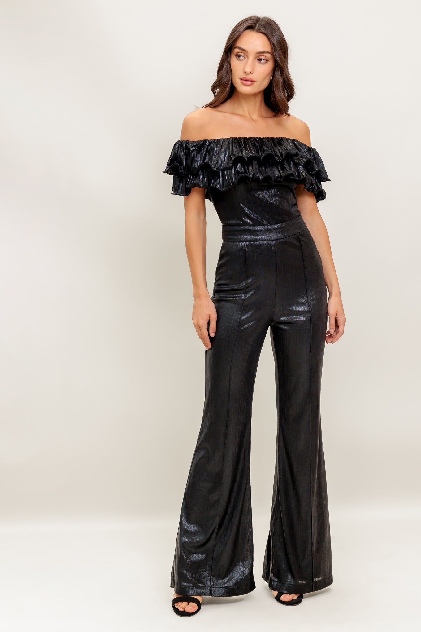 A black coated woven jumpsuit featuring off shoulder neckline, double layer pleated flounce, flare leg and back zipper closure