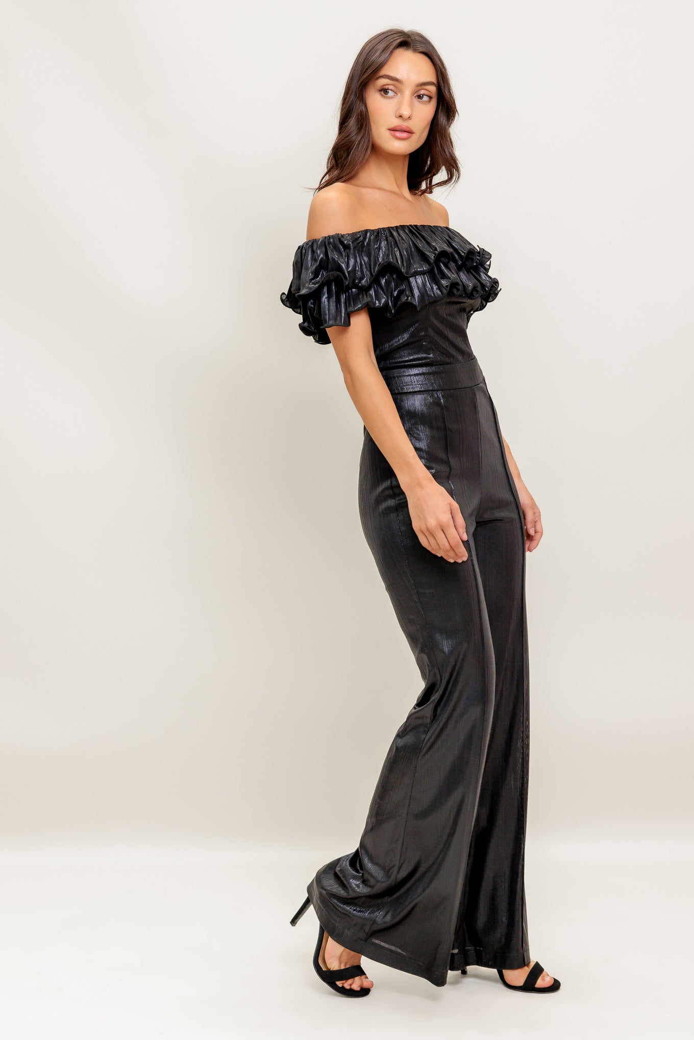 A black coated woven jumpsuit featuring off shoulder neckline, double layer pleated flounce, flare leg and back zipper closure