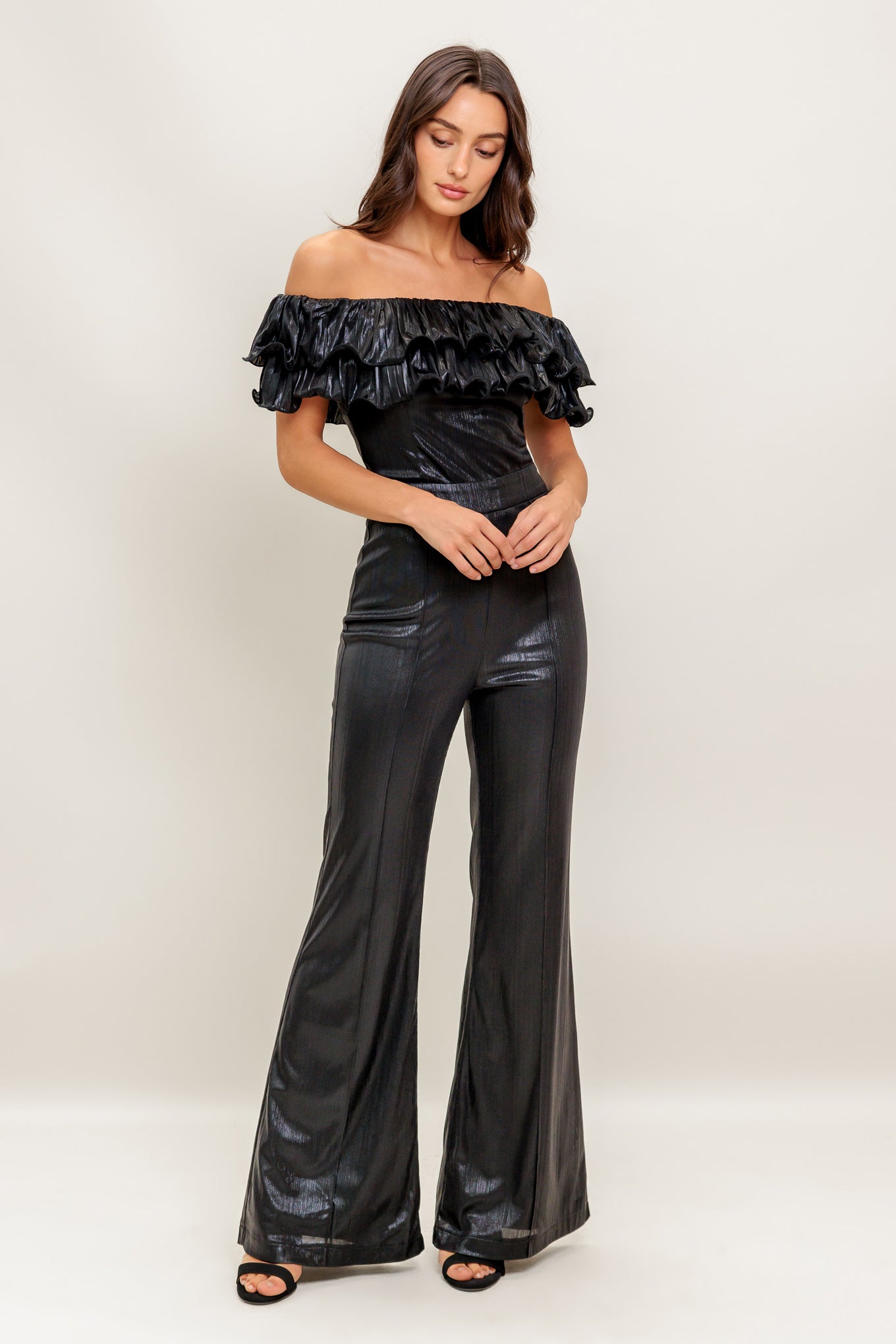 A black coated woven jumpsuit featuring off shoulder neckline, double layer pleated flounce, flare leg and back zipper closure