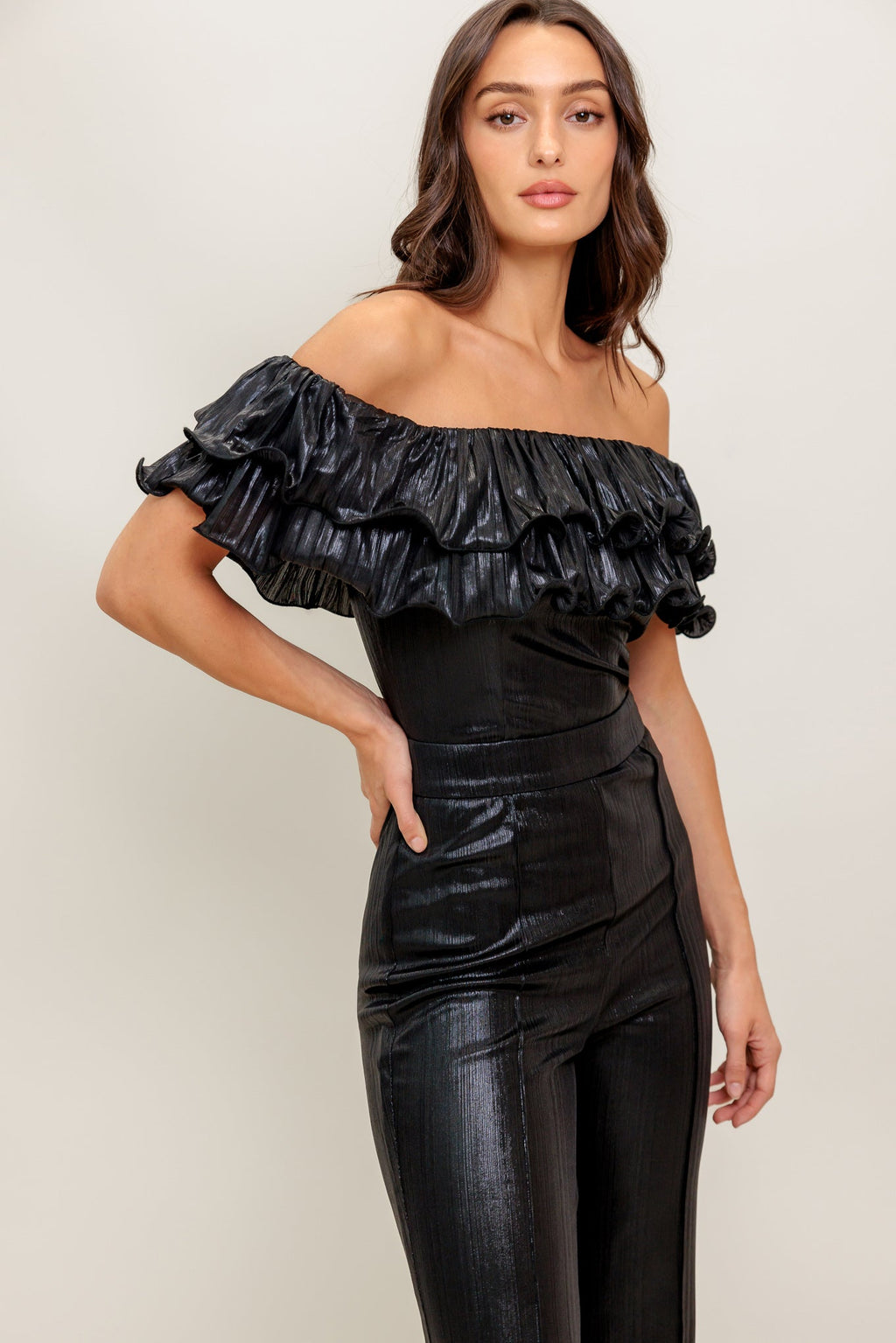 A black coated woven jumpsuit featuring off shoulder neckline, double layer pleated flounce, flare leg and back zipper closure