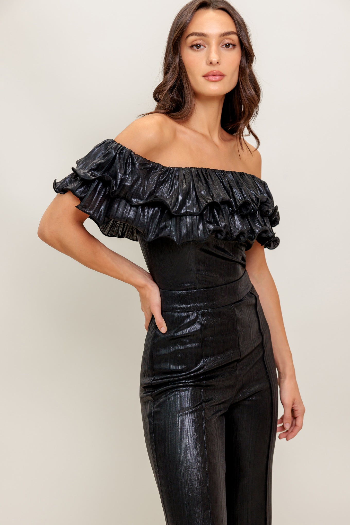 A black coated woven jumpsuit featuring off shoulder neckline, double layer pleated flounce, flare leg and back zipper closure
