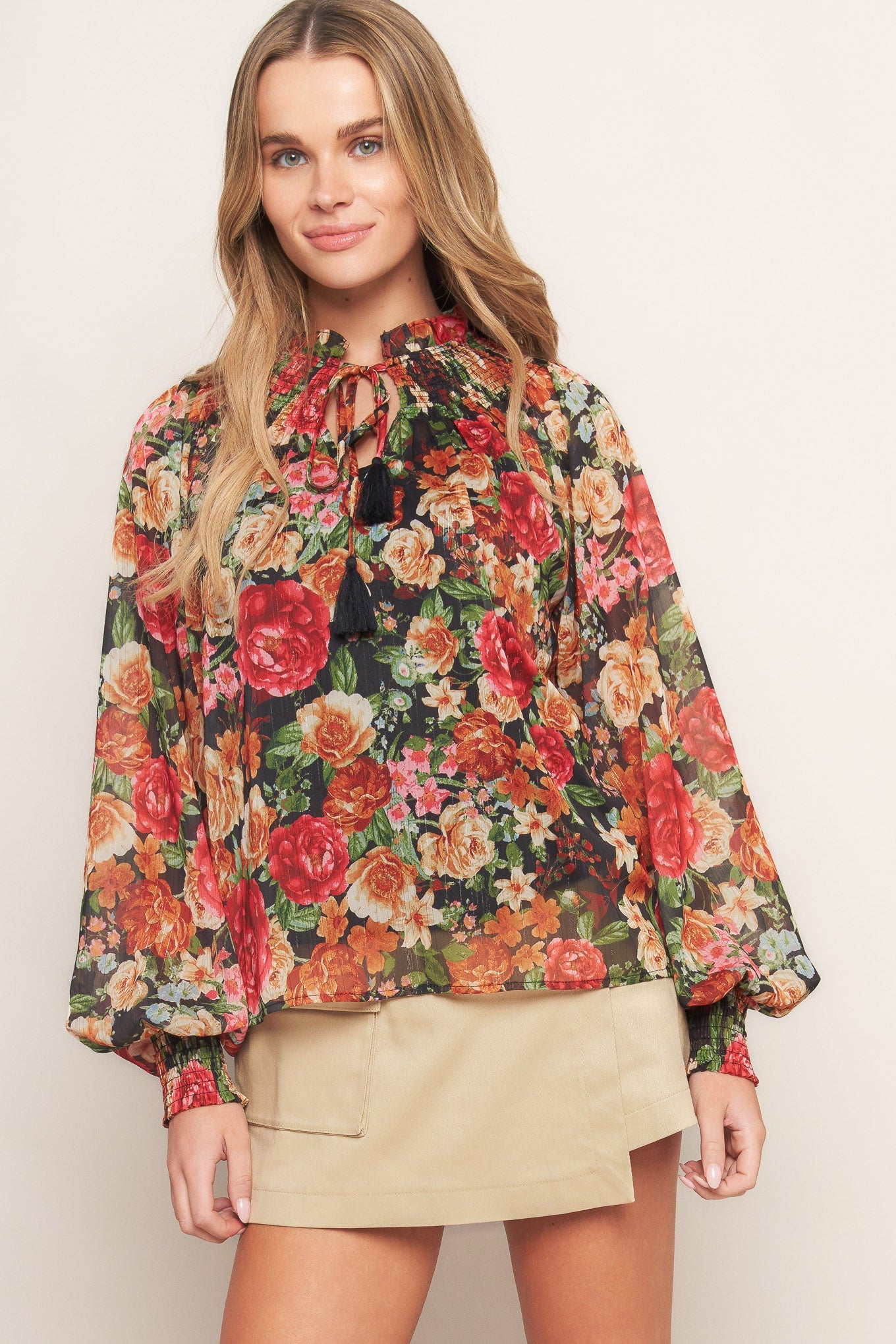 A printed woven top featuring high neckline, peasant sleeve with smocked cuff and front tie detail