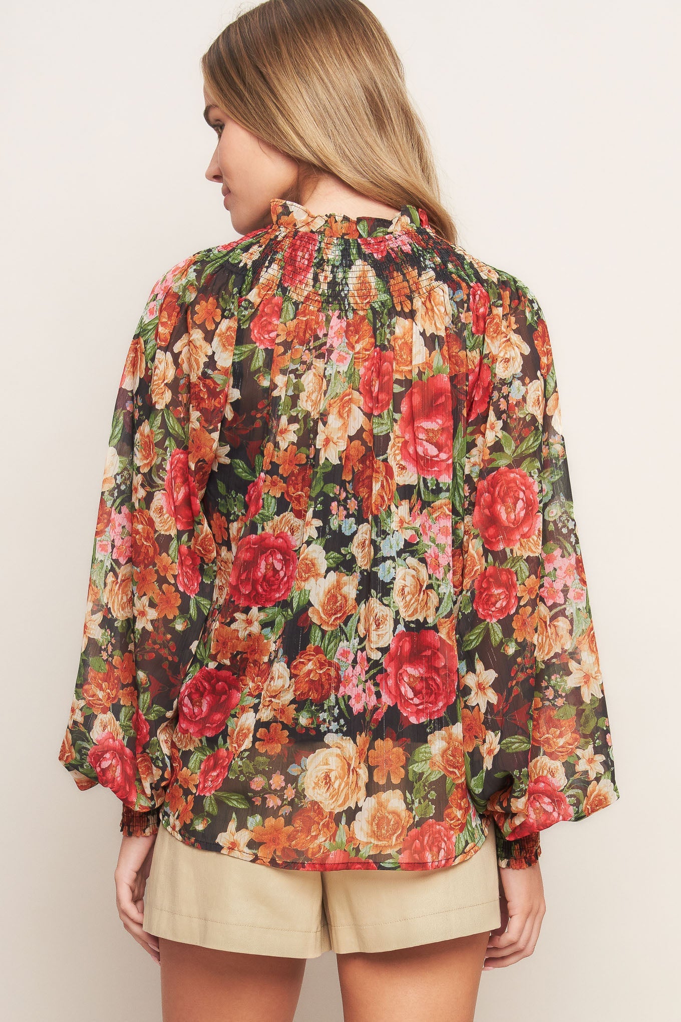 A printed woven top featuring high neckline, peasant sleeve with smocked cuff and front tie detail