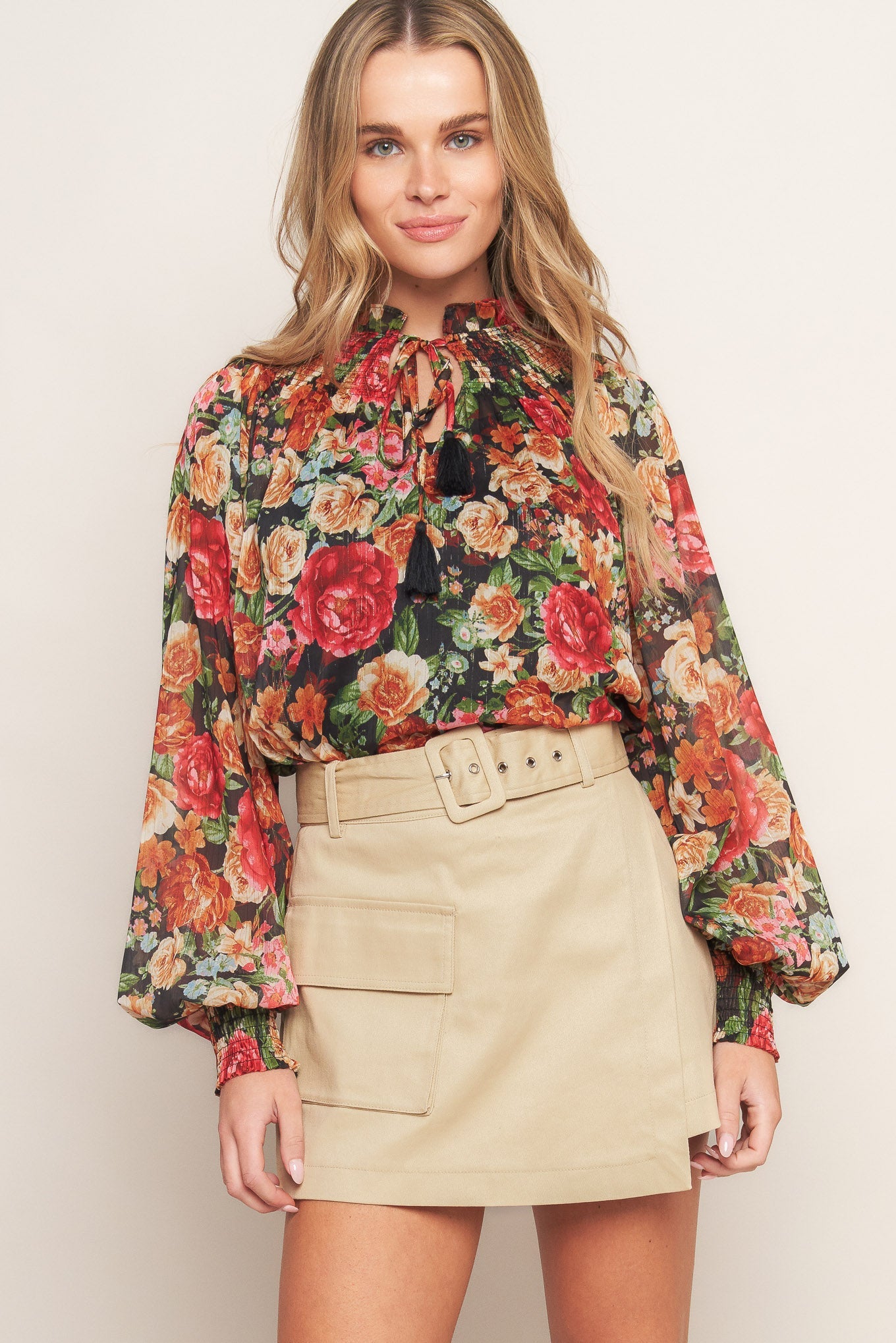 A printed woven top featuring high neckline, peasant sleeve with smocked cuff and front tie detail