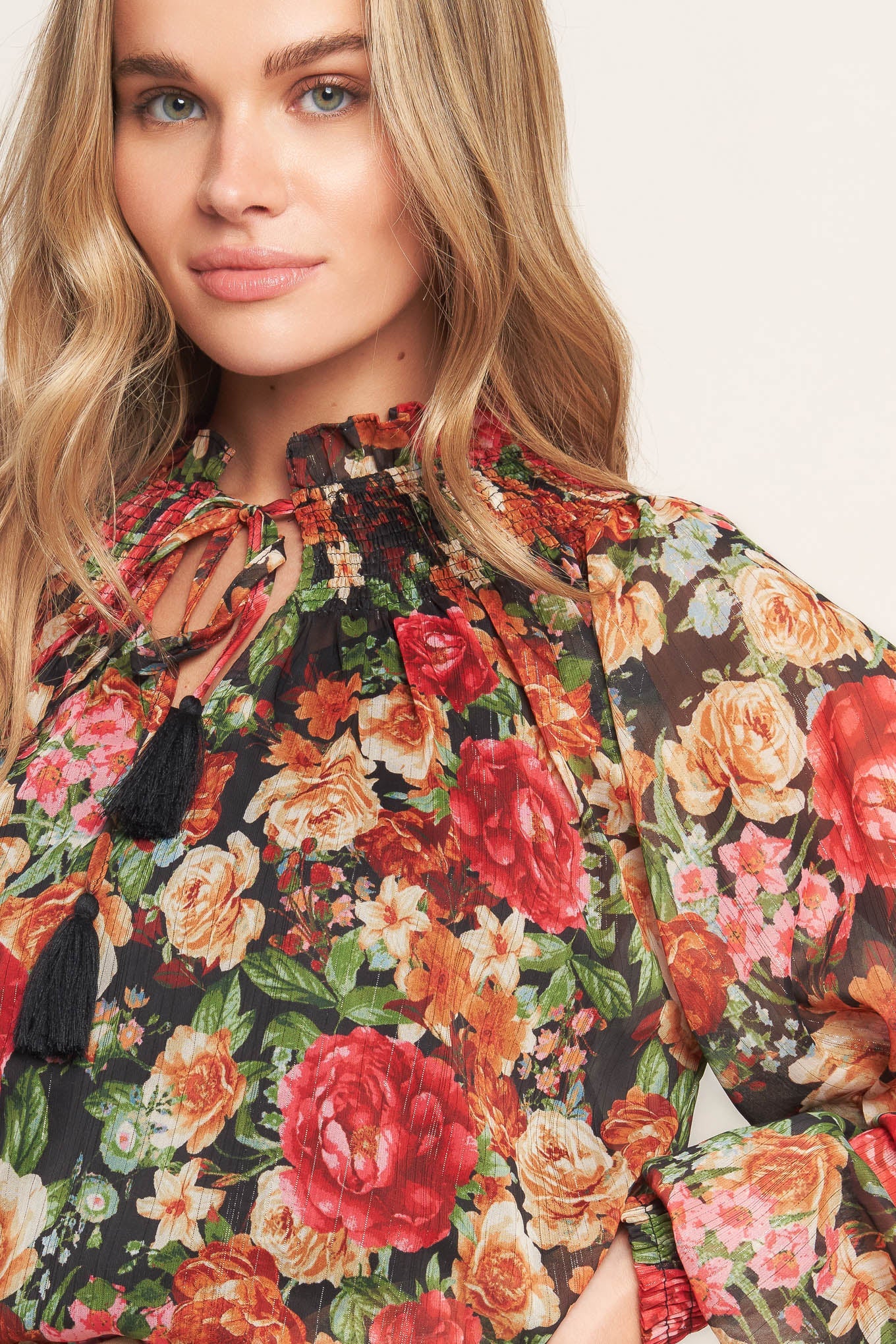 A printed woven top featuring high neckline, peasant sleeve with smocked cuff and front tie detail