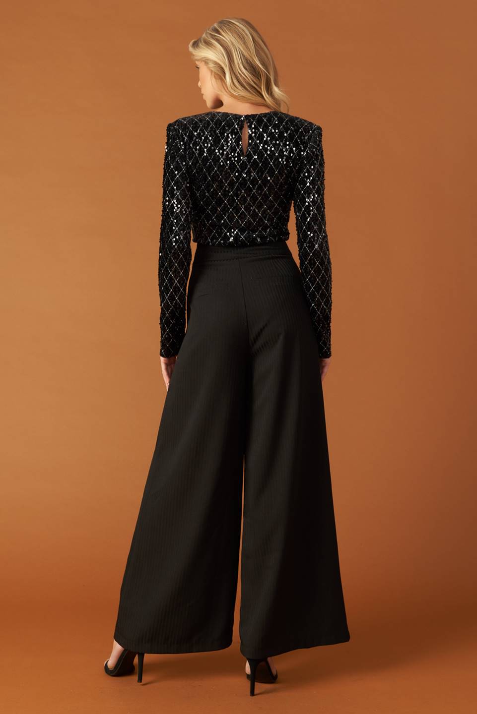 A black sequin bodysuit featuring round neckline, long sleeve and mesh bottom with snap closure.