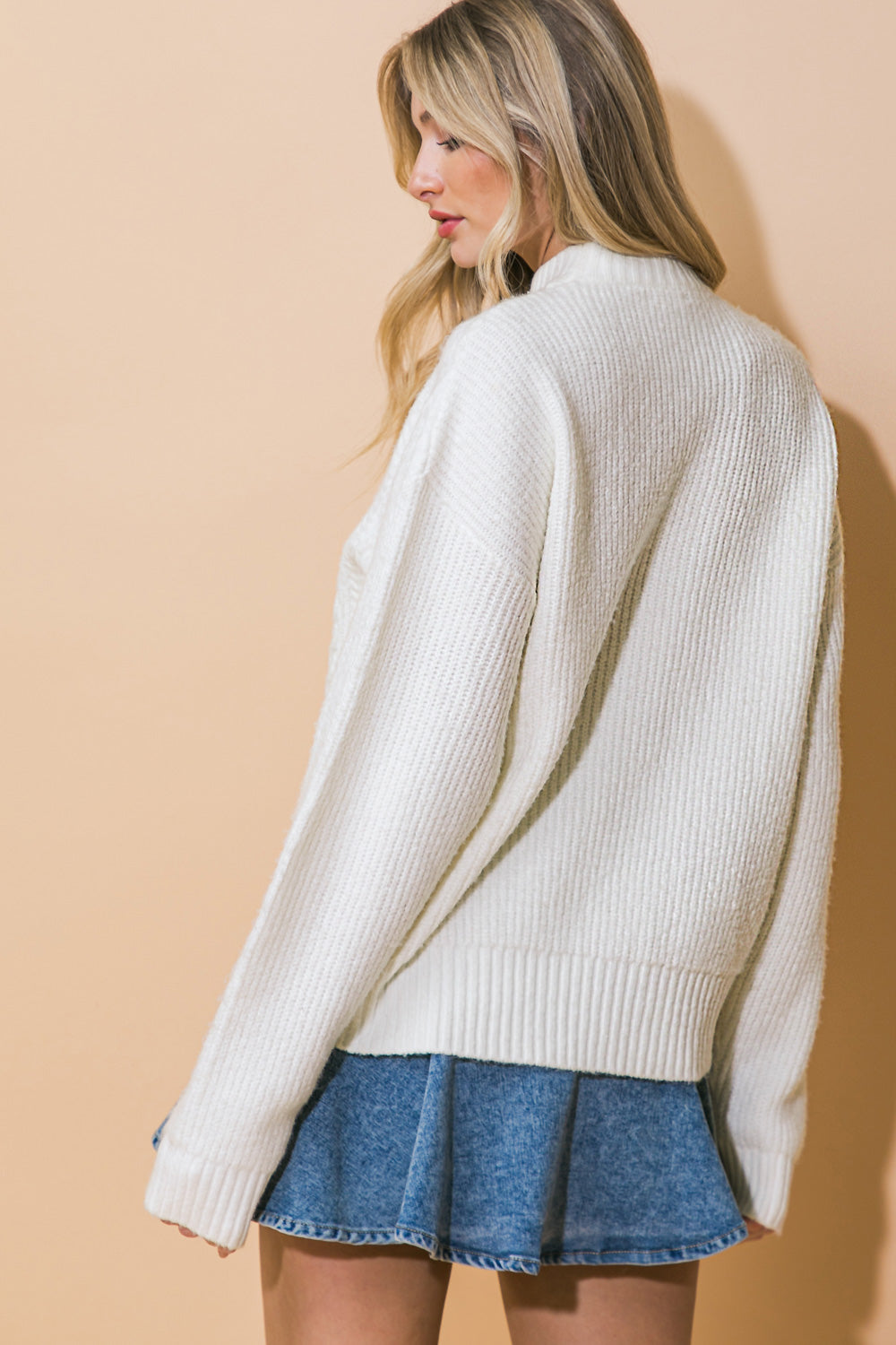 A white knit sweater top featuring mock neck, long sleeve and relaxed body